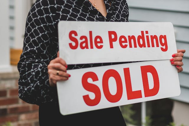 pexels-rdne-8292794 A person holding a "Sale Pending" sign over a "SOLD" sign, indicating a property sale in progress.