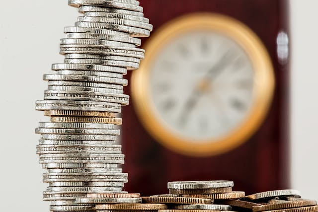 Coins stacked on table with clock in the background
