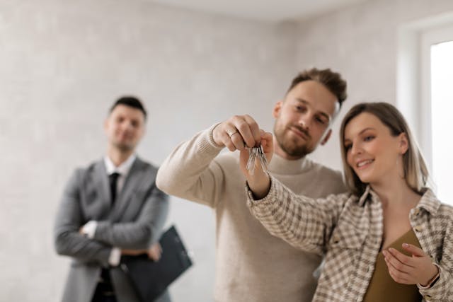 Landlord proudly watching a happy couple holding the keys